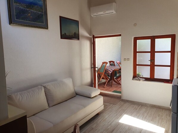 A living room with a beige sofa, a dining table with chairs, a window with frosted glass panes, and a door leading outside. - Apartment Kova (Stari Grad)