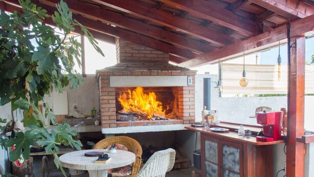 An outdoor patio with a brick pizza oven, wicker furniture, and a bar area. - Apartment Kova (Stari Grad)