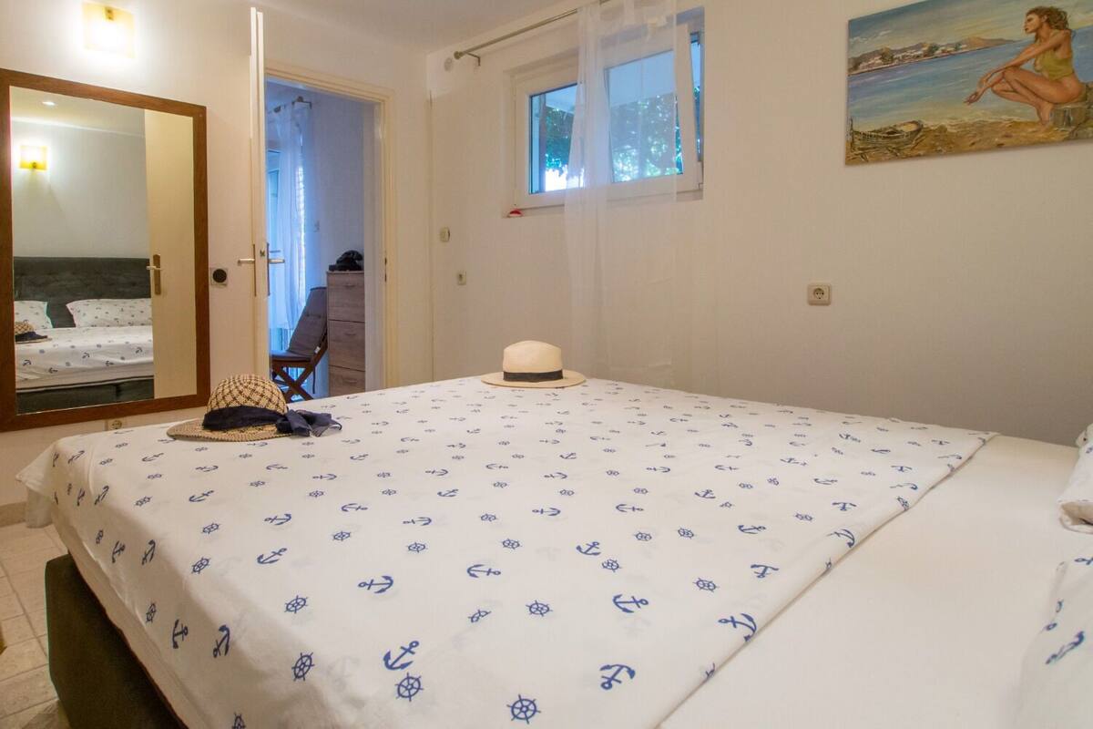 A bedroom with a bed, a mirror, a window with curtains, a painting, and a door leading to another room.