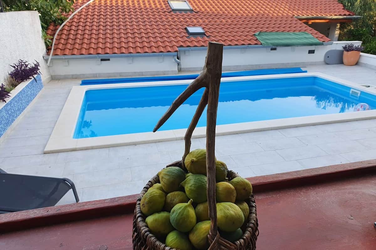 A swimming pool with a tiled roof and a basket of green fruits on a balcony.