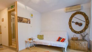 A cozy living room with a white sofa, colorful pillows, a small table with a basket, a violin on a mirror, and a suitcase on a cabinet. - Apartment Kova (Stari Grad)