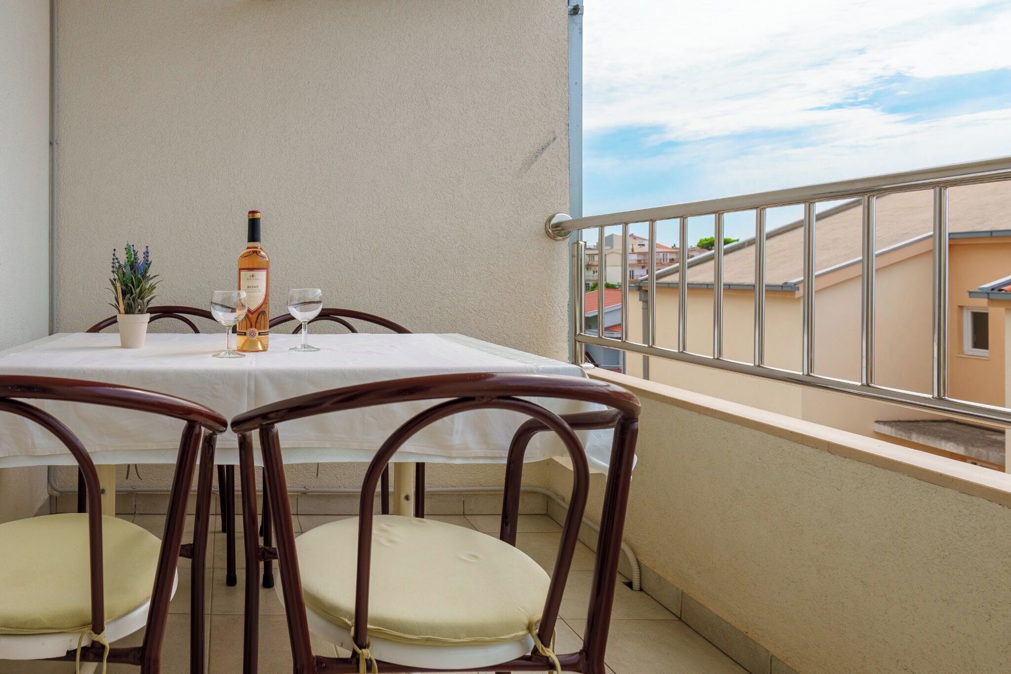 Un balcón con una mesa dispuesta para dos personas, una botella de vino y una pequeña planta en maceta.