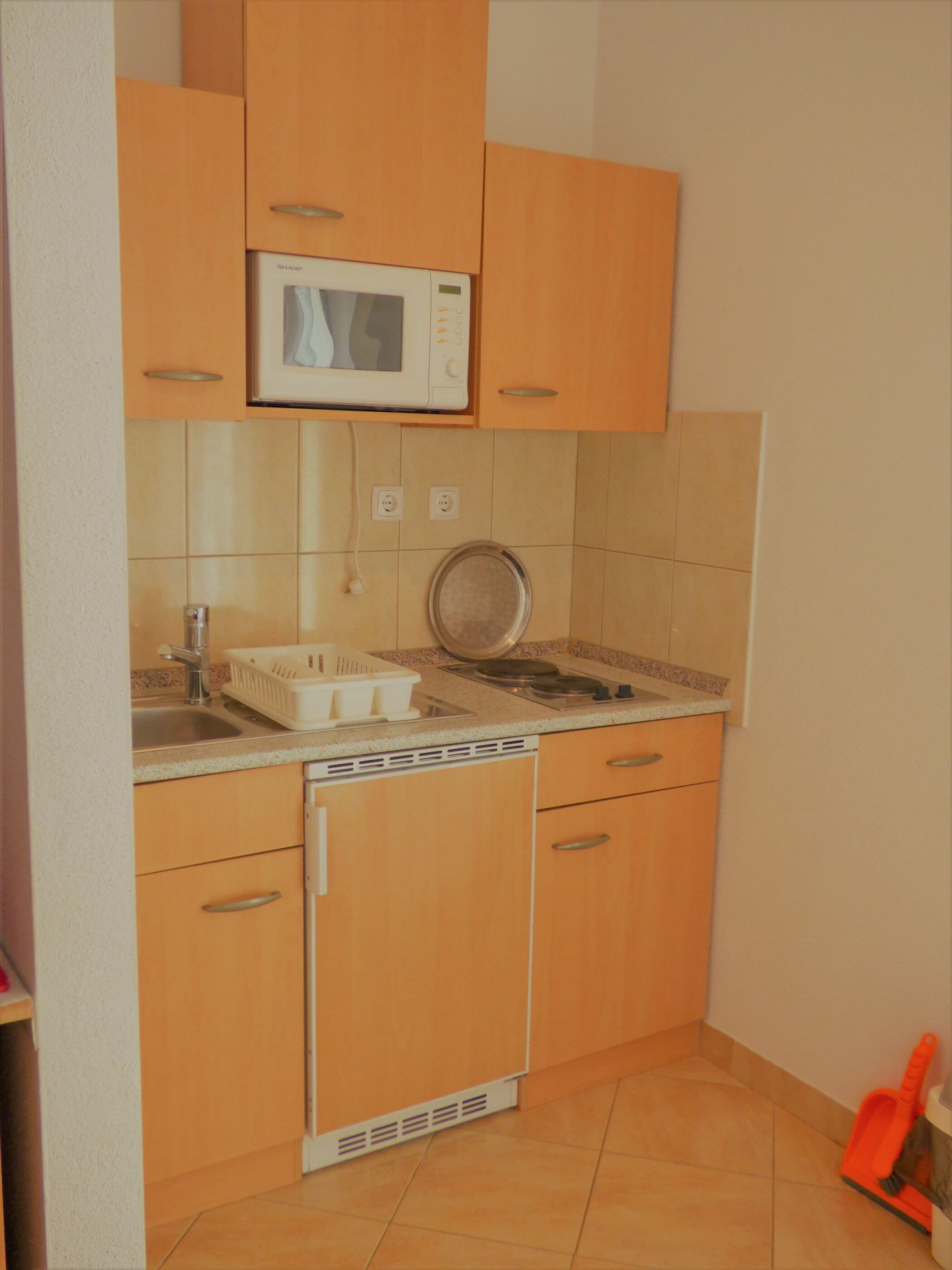 A compact kitchen with wooden cabinets, a microwave, a sink, and a dishwasher.