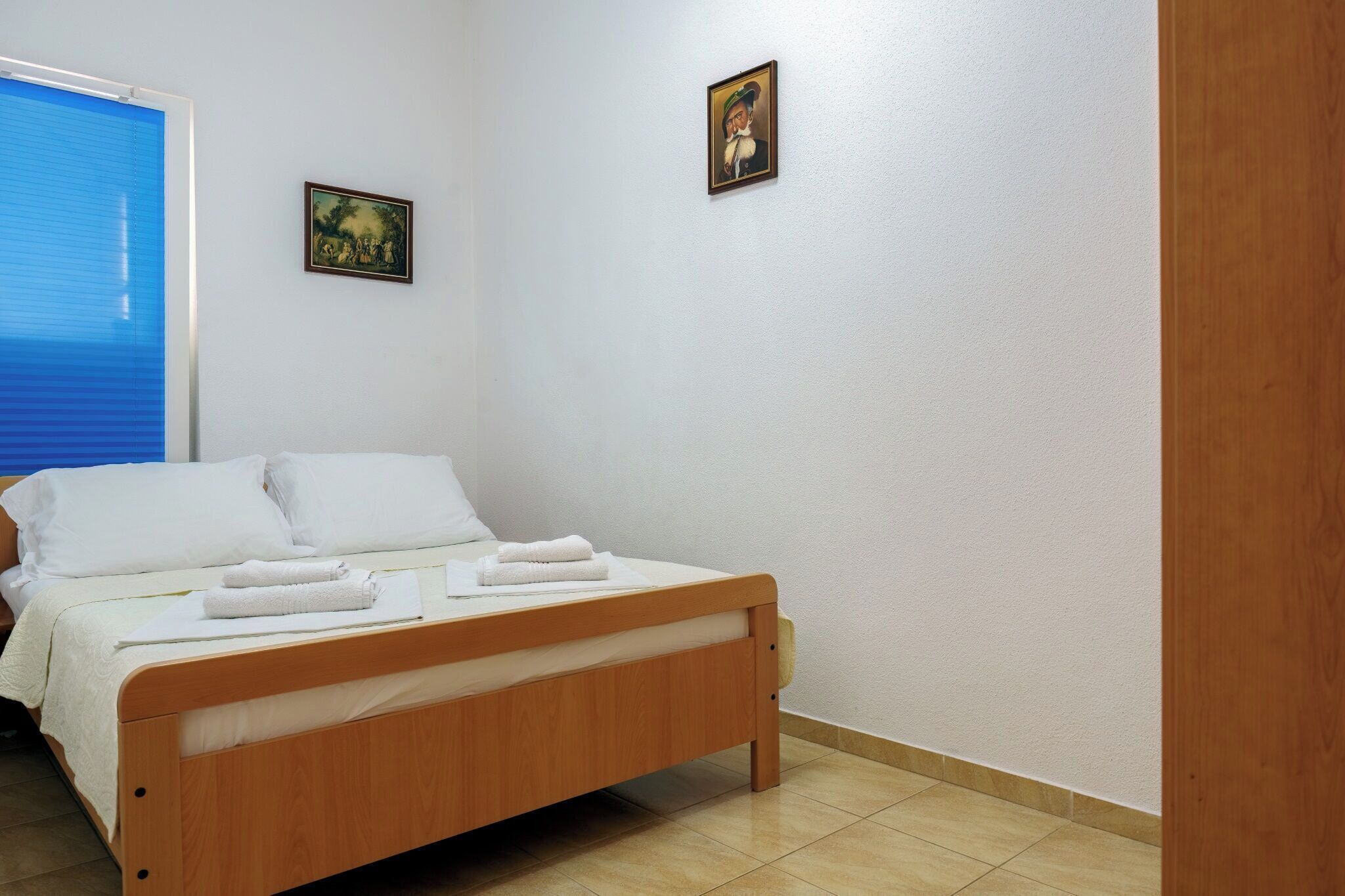 A neatly made bed with white linens and towels, a wooden headboard, and two framed pictures on the wall.