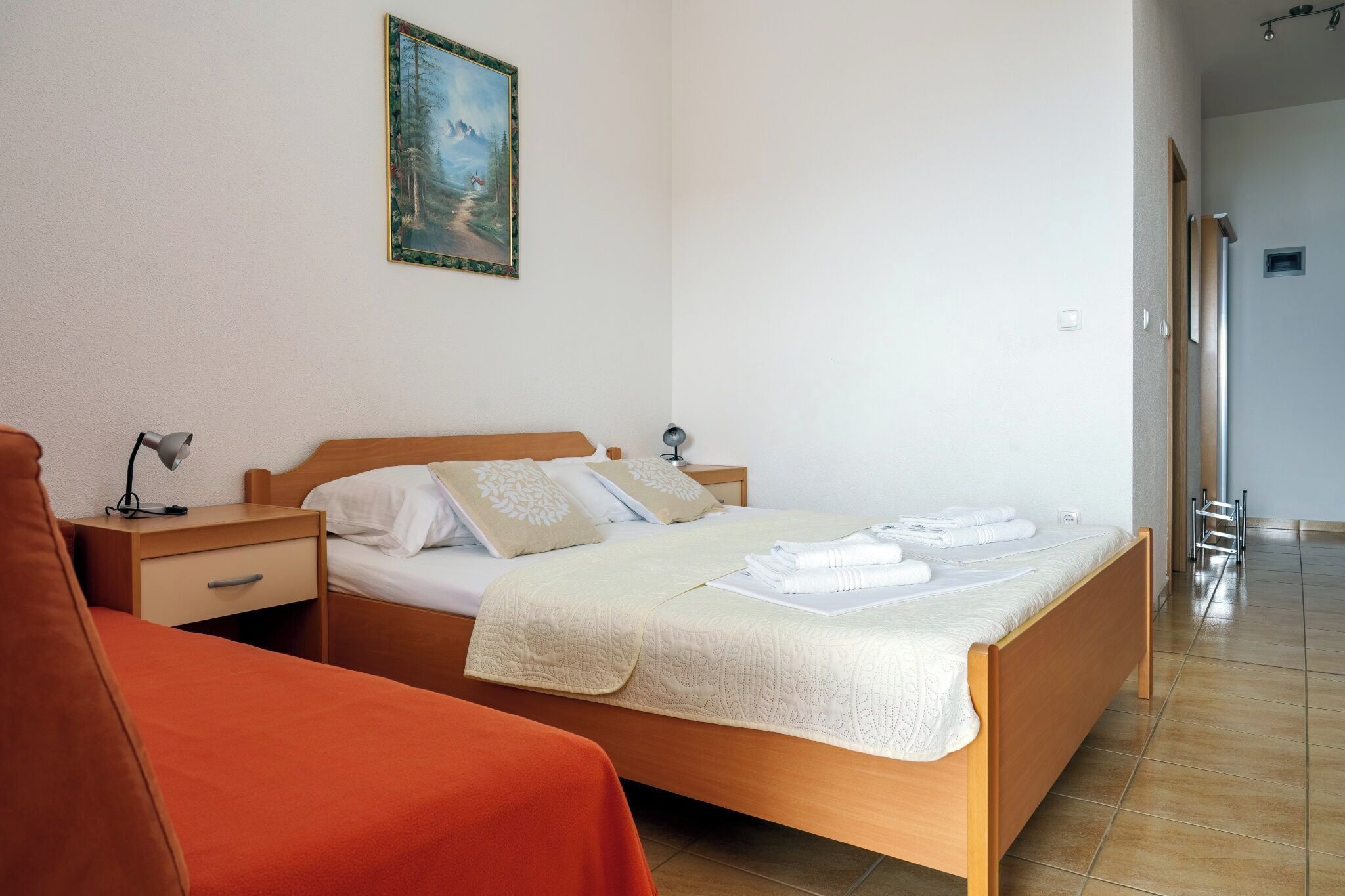 Un dormitorio con cama de madera, mesita de noche, escritorio, silla y un cuadro en la pared.