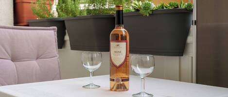 A bottle of rosé wine on a table with two glasses, surrounded by potted plants.