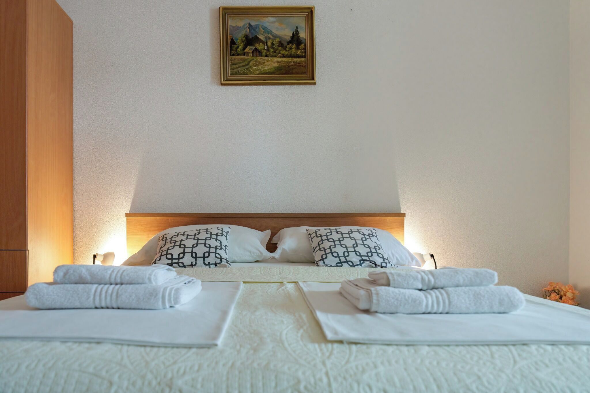 A hotel room with a bed, two pillows, a painting on the wall, and towels on the bed.
