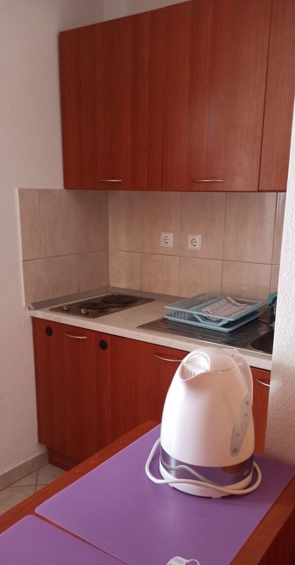 A compact kitchen with wooden cabinets, a countertop, and a kettle on a purple mat. - Apartments "ruza" Baska Voda (Baska Voda)