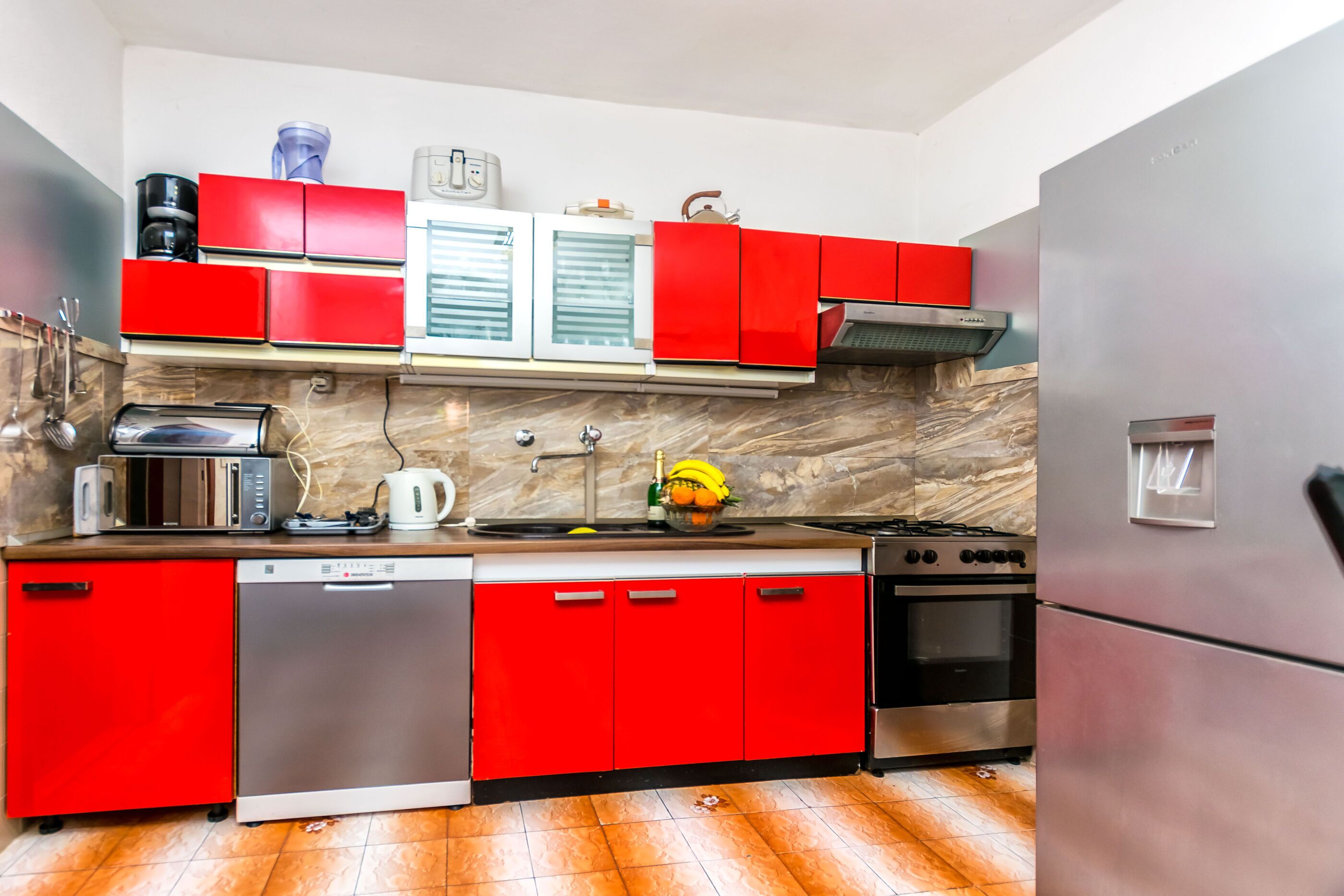 A modern kitchen with red cabinets, stainless steel appliances, and a marble backsplash.