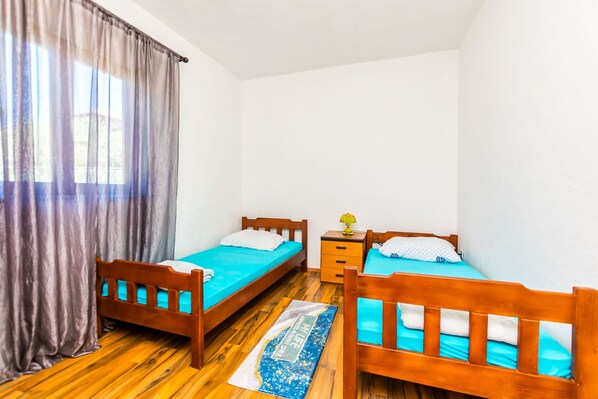 A room with two wooden beds, a small nightstand, and a window with curtains. - Apartment Jadranka (Supetar)