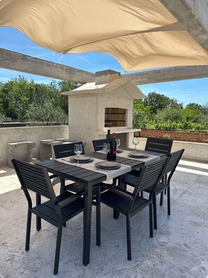 An outdoor patio with a table set for dining, a built-in pizza oven, and a large canopy providing shade. - House Cord Dugopolje (Dugopolje)