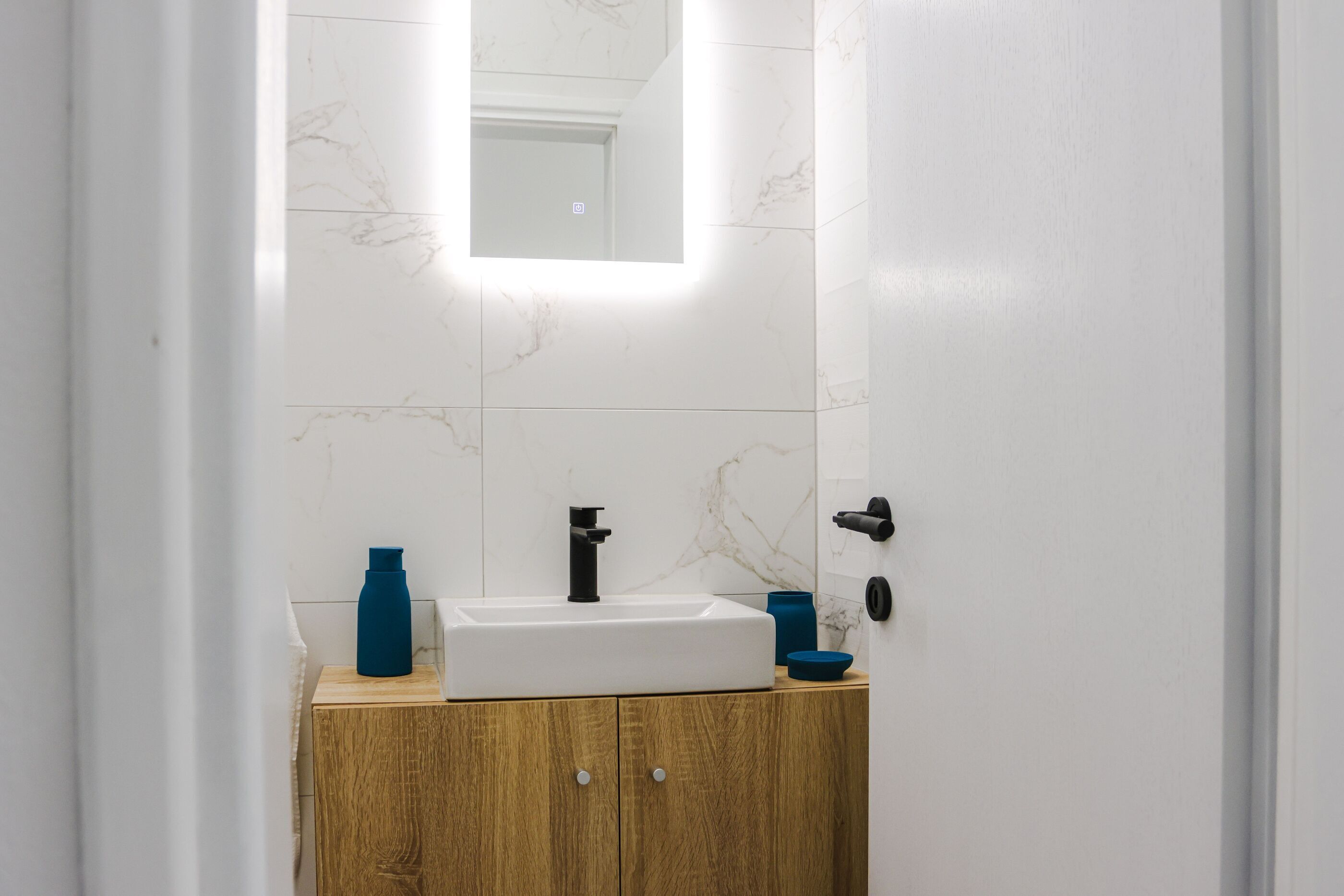 Un bagno con lavandino bianco, mobiletto in legno e specchio.