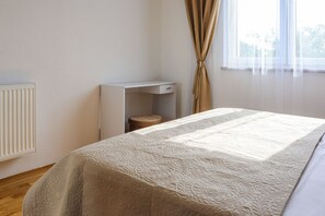 Quarto com cama, mesa de cabeceira, radiador e janela com cortinas.