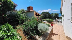 A garden with a variety of plants and flowers, a brick chimney, and a clear blue sky. - Apartment Emma (Novi Vinodolski)