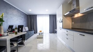 Una cocina moderna con horno y microondas integrados, una zona de comedor con un sofá y una mesita, y un ventanal con cortinas.