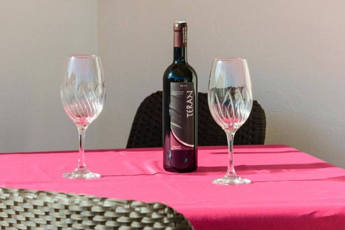 A bottle of Teran wine and two glasses on a table with a pink tablecloth.