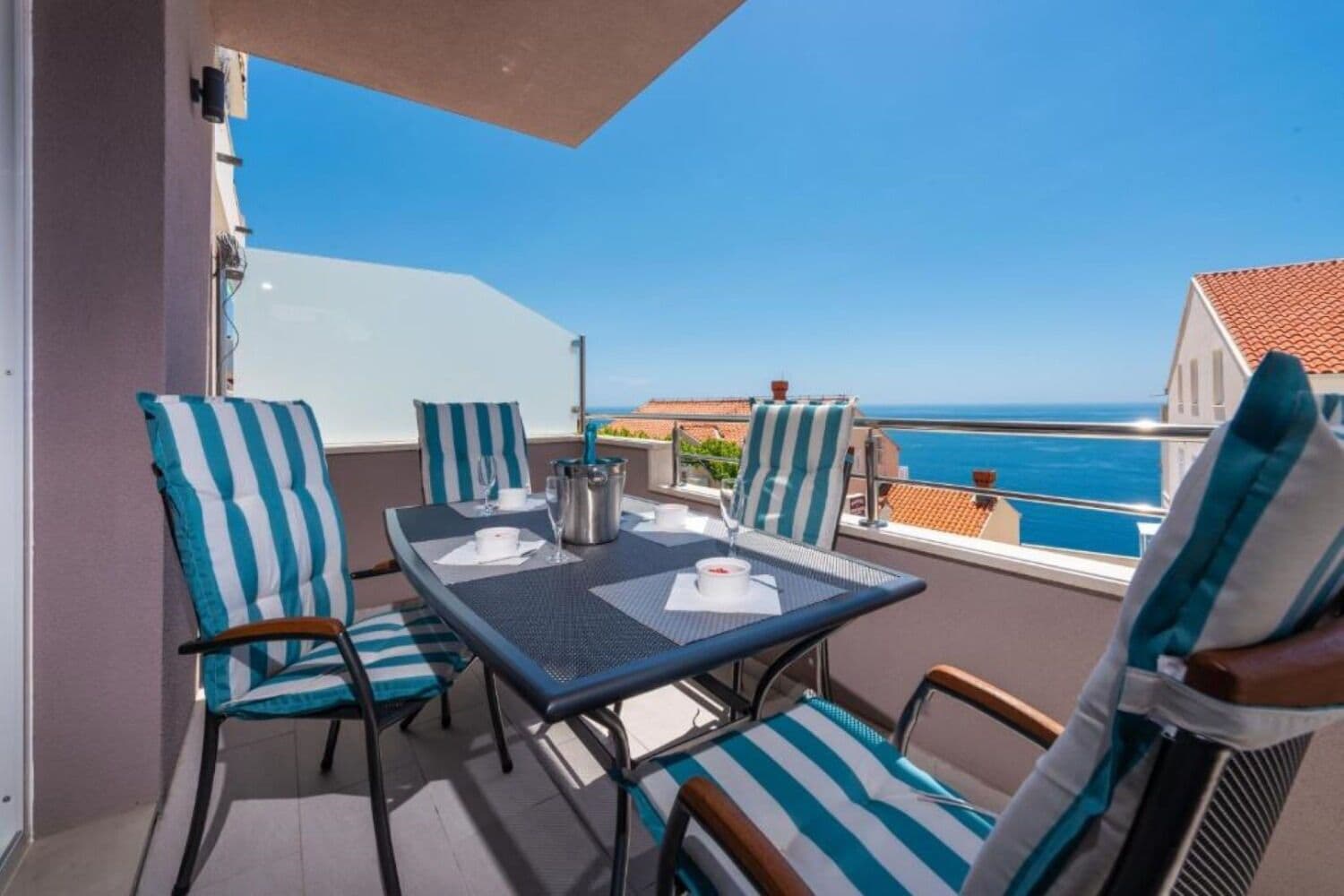 Ein Balkon mit Tisch für zwei Personen, gestreiften Stühlen und Blick auf das Meer.