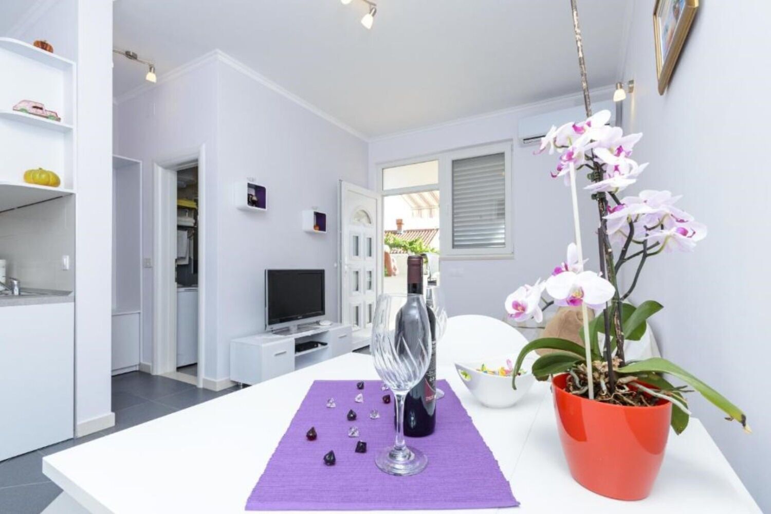 Una sala de estar moderna con un sofá blanco, un televisor, una copa de vino y objetos decorativos sobre una mesa.