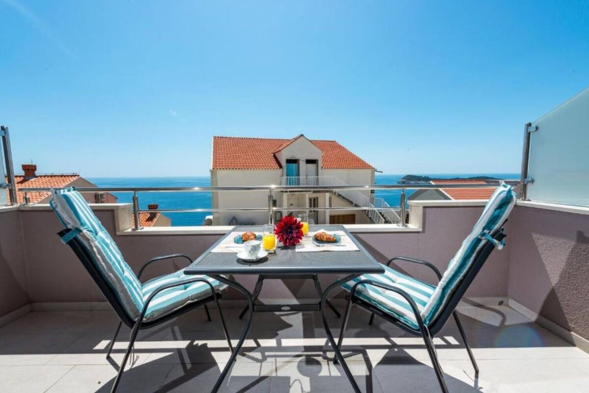 A balcony with two chairs, a table, and a breakfast setting overlooking the sea.
