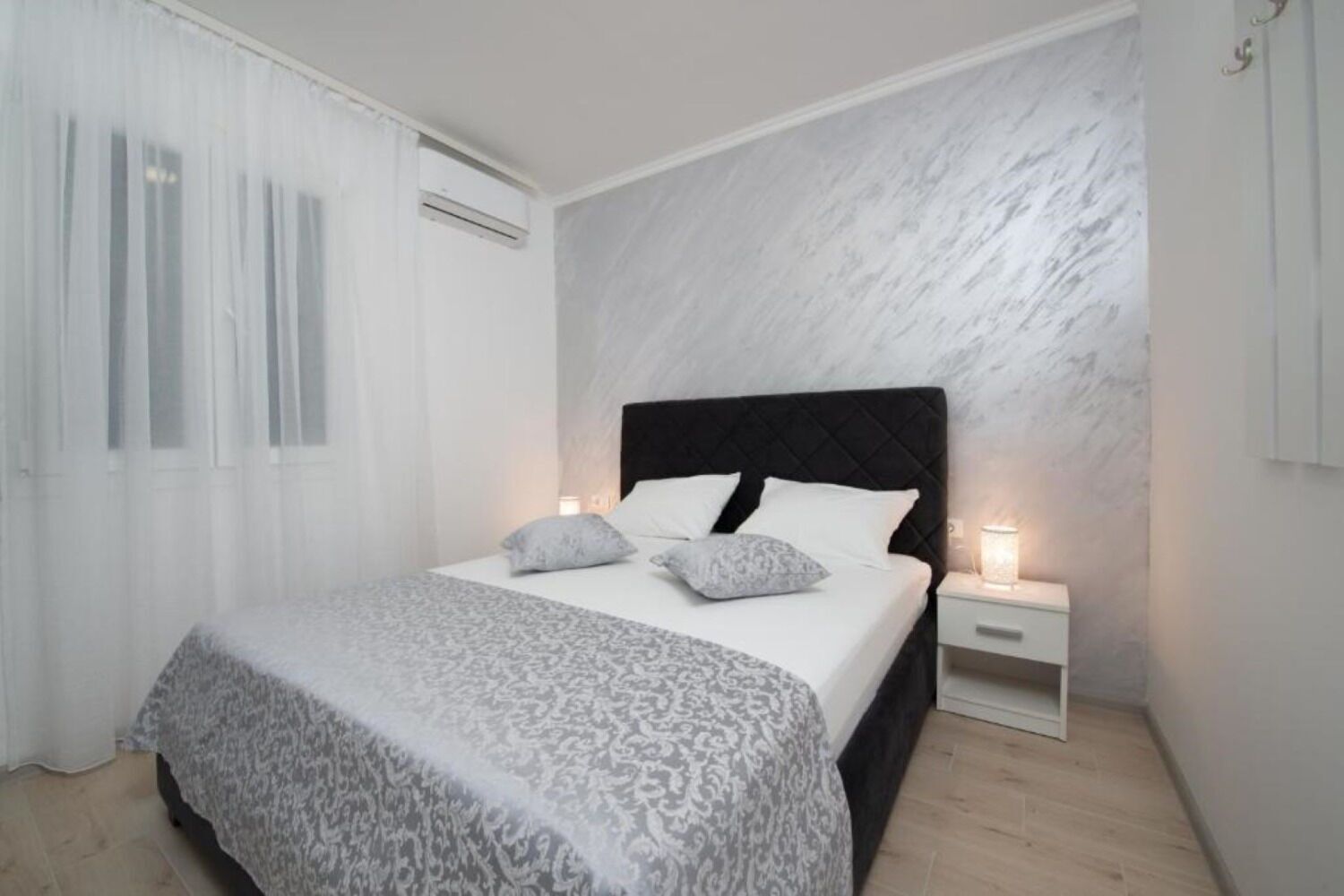Ein Schlafzimmer mit einem Bett, weißen Vorhängen, einer Marmorwand und einem Nachttisch mit einer Lampe.