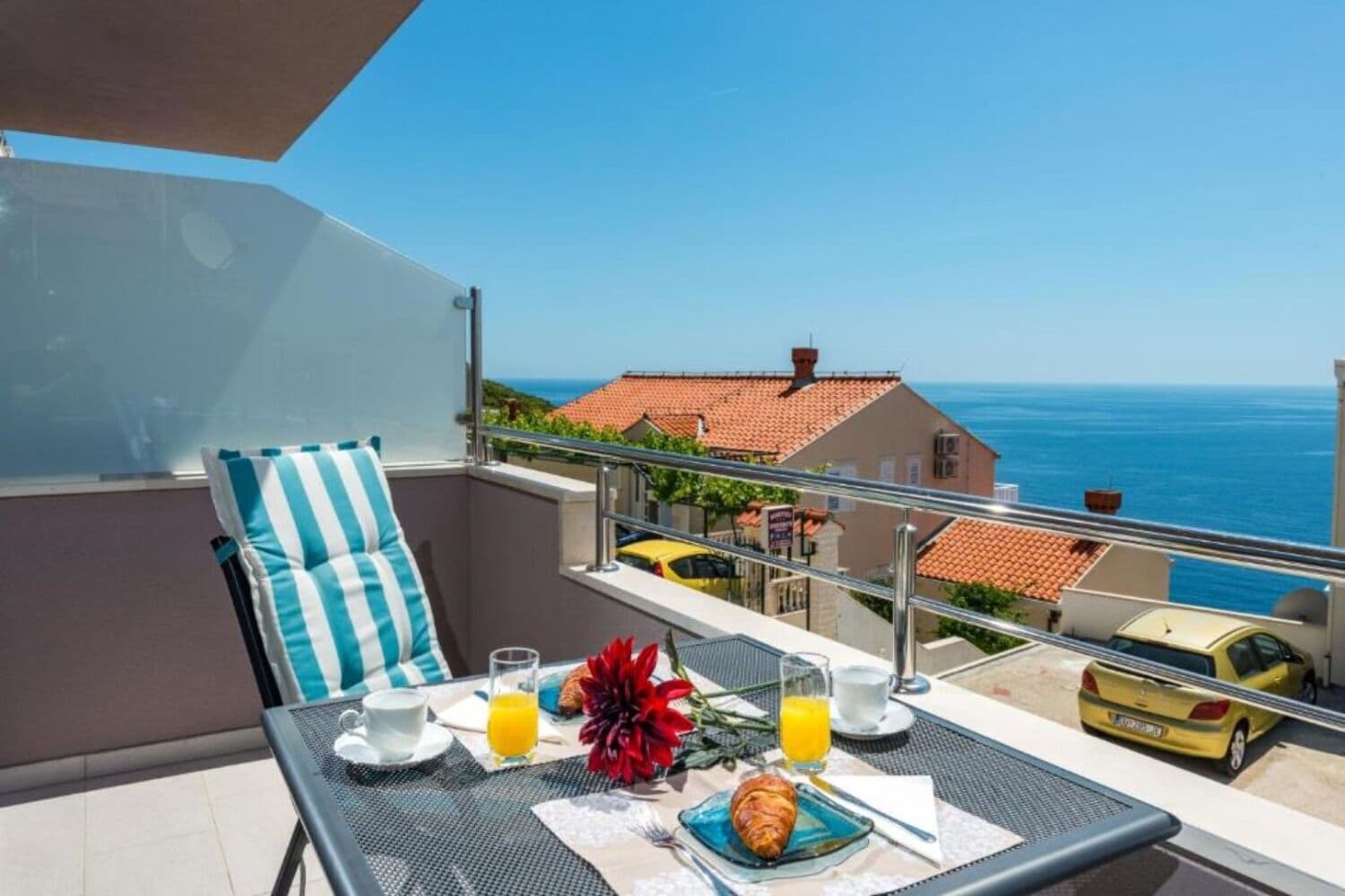 A balcony with a table set for breakfast, a chair, and a view of the sea and buildings.