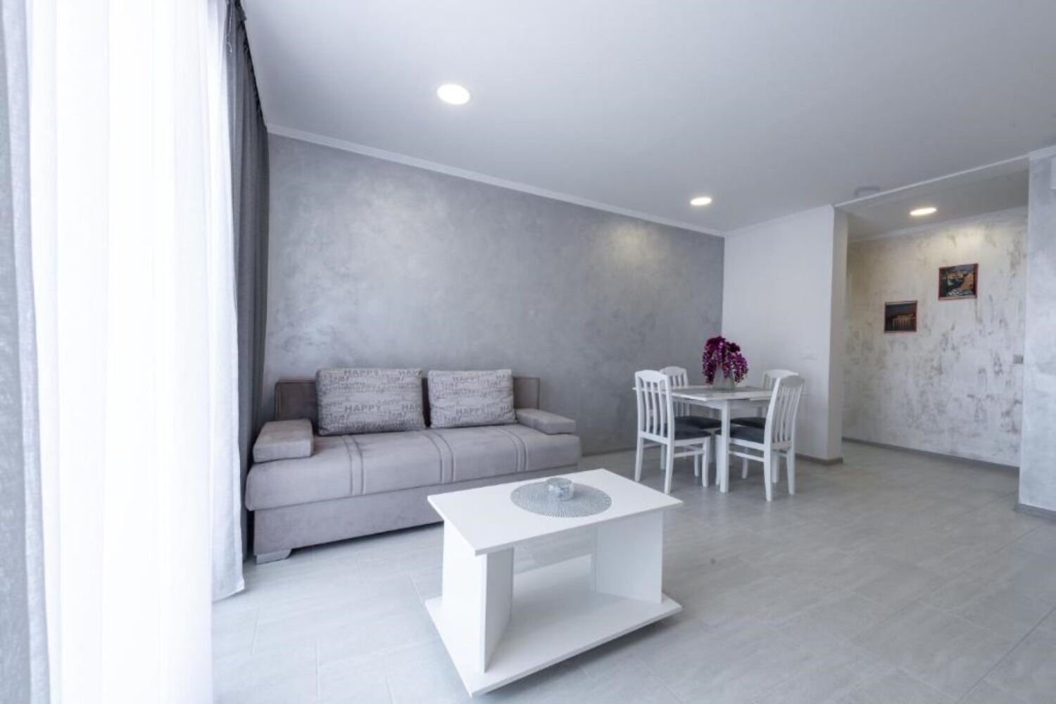 Ein modernes Wohnzimmer mit grauem Sofa, weißem Esstisch und Stühlen.