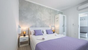 Una habitación de hotel moderna con una cama grande, un armario y una mesita de noche con lámpara.