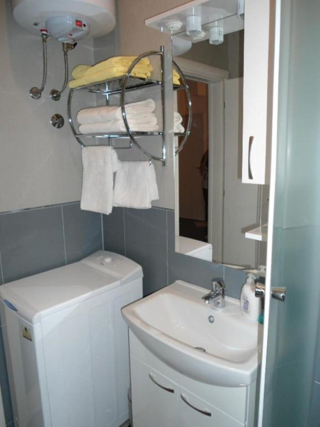 Une salle de bain avec un lavabo blanc, un miroir et un porte-serviettes sur lequel sont pliées des serviettes.