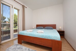Ein Schlafzimmer mit einem hölzernen Bett, einem Nachttisch, einer Schiebetür aus Glas und Blick auf Grünfläche außerhalb.