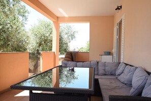 Ein Balkon mit einem Glastisch, einem grauen Sofa und Blick auf Bäume und Gebäude.