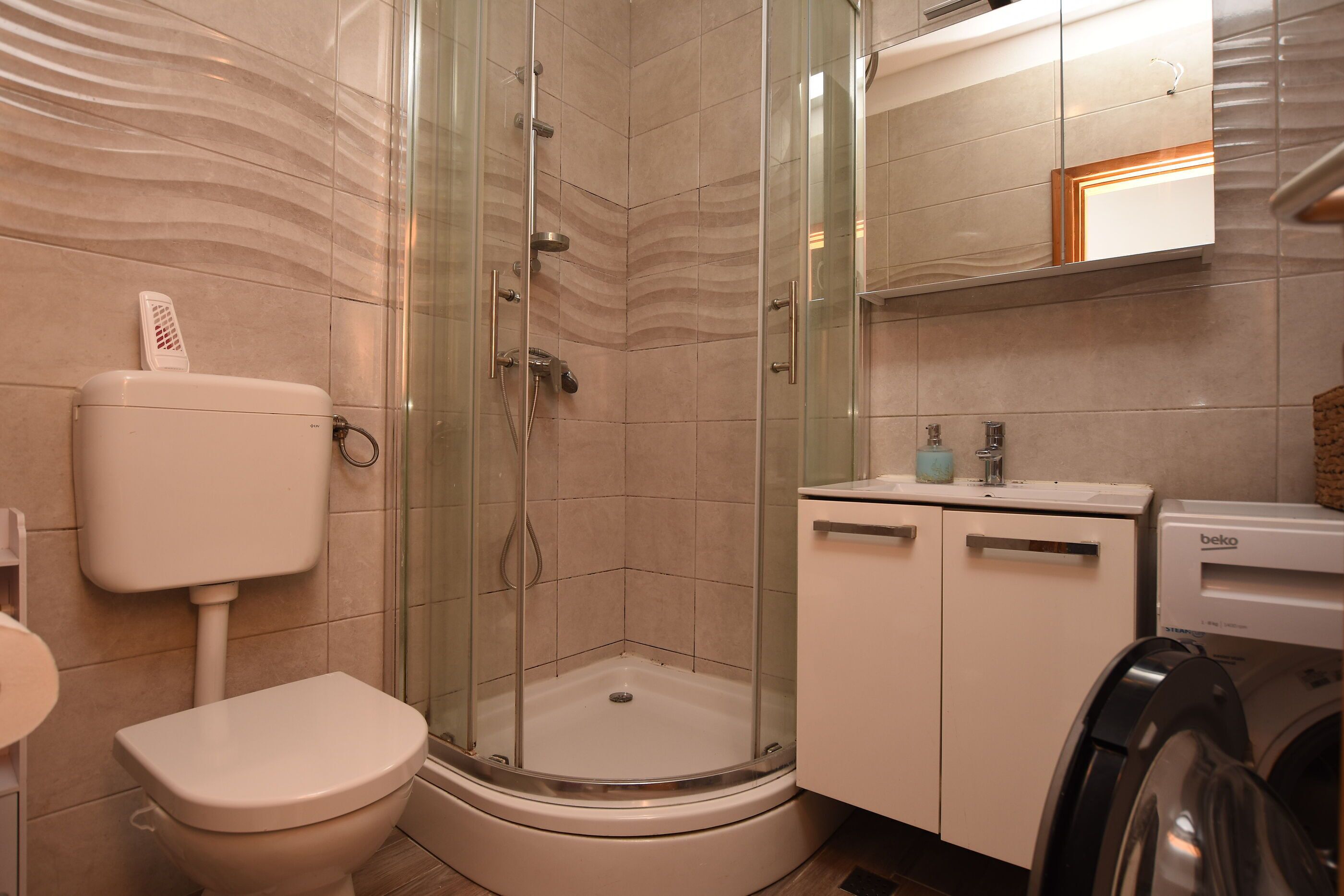 A bathroom with a glass-enclosed shower, a toilet, a sink, and a washing machine.