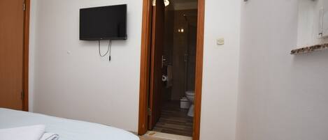 A bedroom with a bed, a television mounted on the wall, and a door leading to a bathroom.