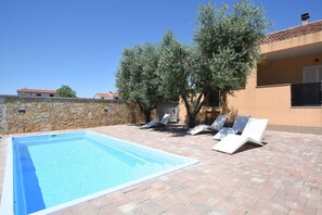 En swimmingpool med solstolar, en stenmur och träd.