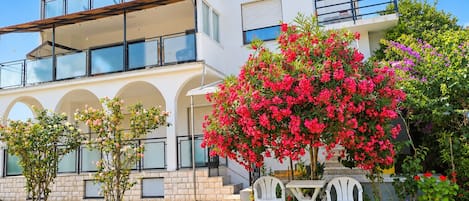 Une maison à deux étages avec un balcon, un jardin agrémenté de plantes en fleurs et un espace salon extérieur.