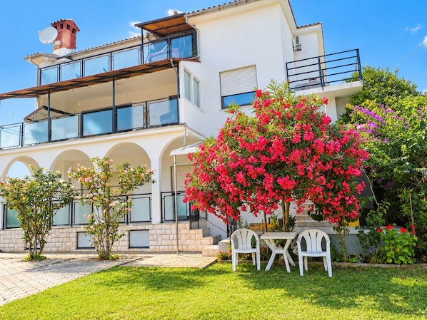 A two-story house with a balcony, a garden with flowering plants, and outdoor seating. - Apartments Tomy (Medulin)