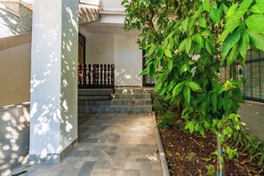 A paved pathway leading to a building entrance with a metal gate, surrounded by greenery and a stone wall. - Apartments Tomy (Medulin)