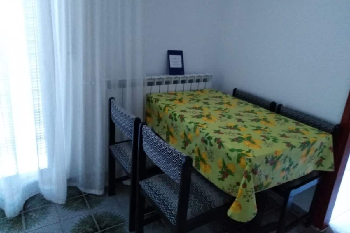 A small dining area with a table covered by a floral tablecloth, a chair, and a radiator.