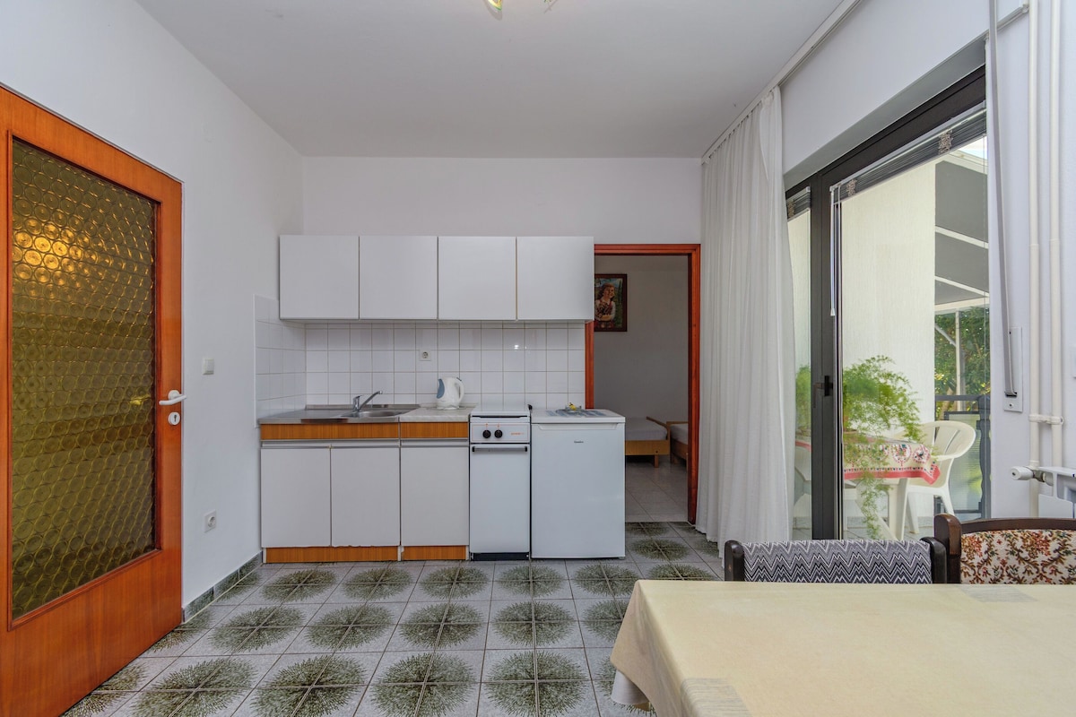 A compact kitchen with white cabinets, a sink, and a stove. There is a dining area with a table and chairs.