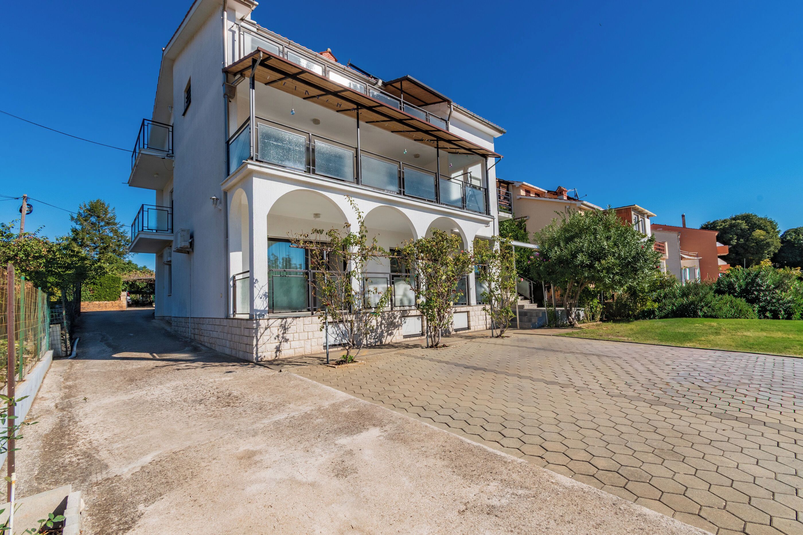 A two-story residential building with a balcony, a paved driveway, and a clear blue sky.