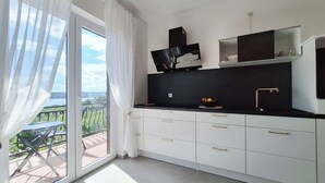 Una cucina moderna con mobili bianchi, un piano di lavoro nero e vista su un balcone con tavolo e sedie.