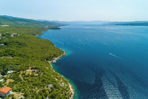 Luftaufnahme einer Küstenregion mit klarem, blauem Meer, grünen Hügeln und verstreuten Gebäuden.