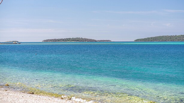 A beach with clear turquoise water, a sandy shore, and distant islands. - Apartments Brodarica Beach (Sibenik)