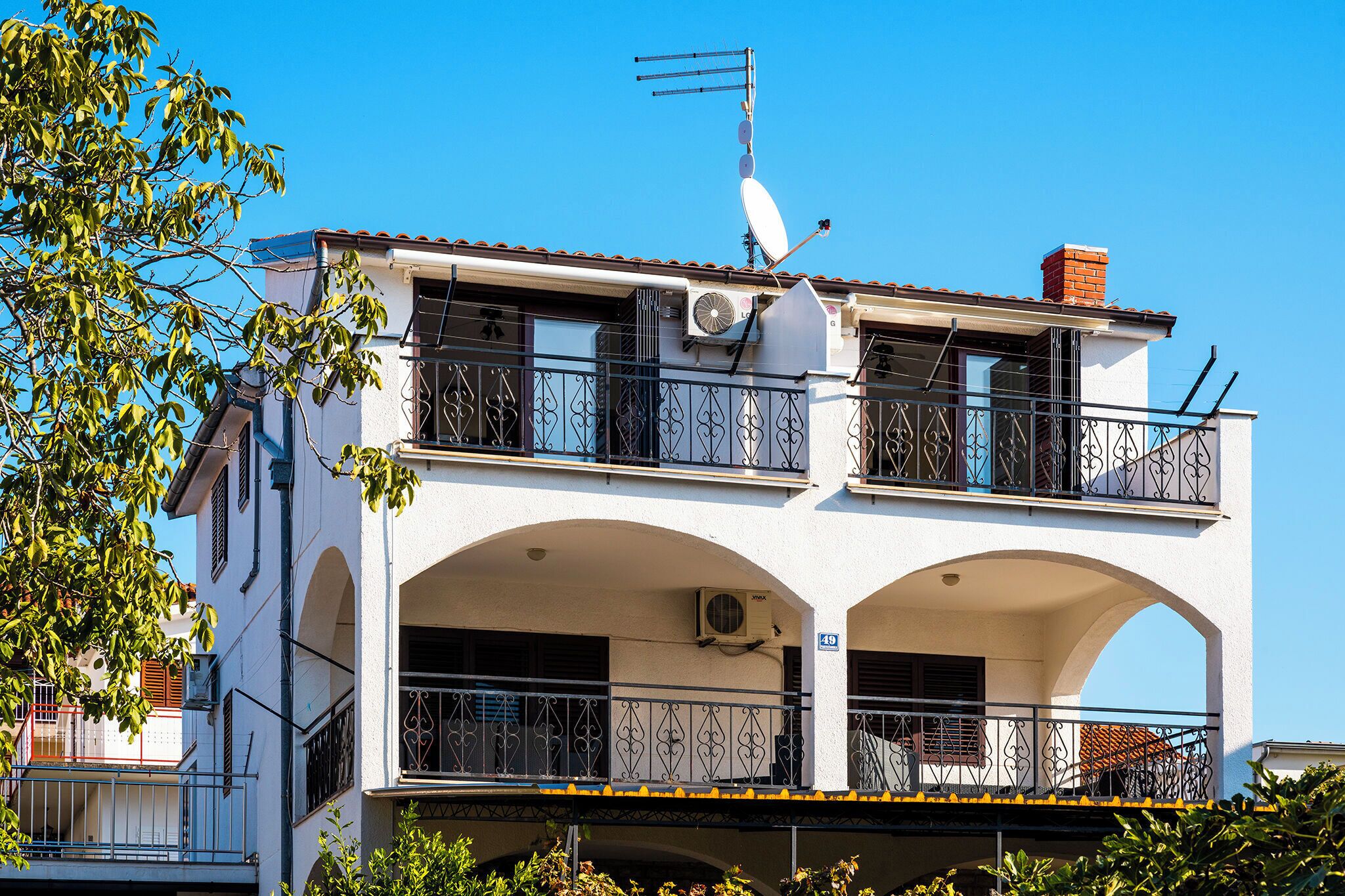 A two-story building with balconies, a satellite dish, and an air conditioning unit.