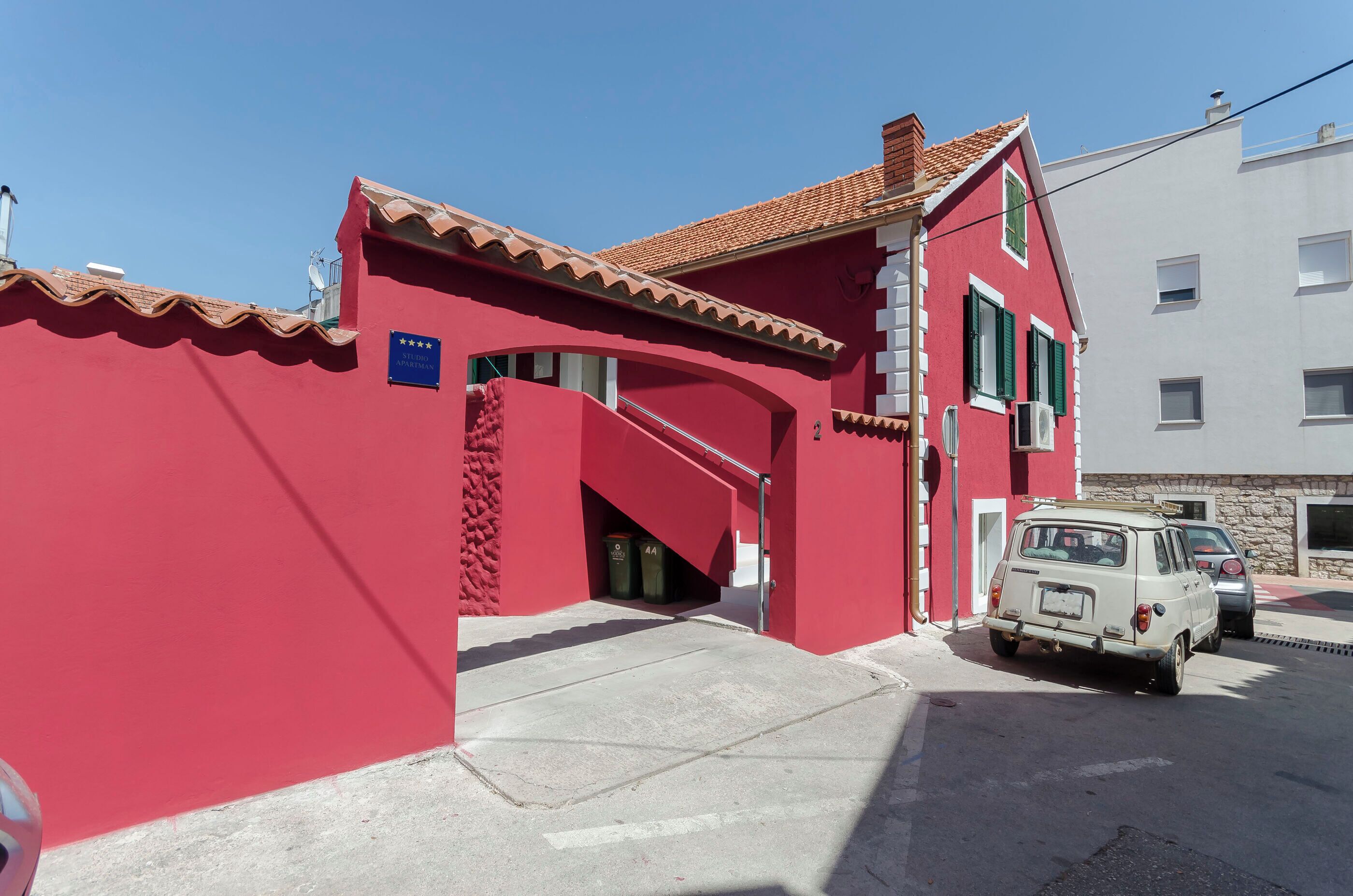 A red building with a blue sign, a staircase, and a parked car.