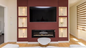 A modern living room with a flat-screen TV mounted on a red wall, surrounded by shelves with decorative items. - Apartment Oldtown With Parking (Vodice)