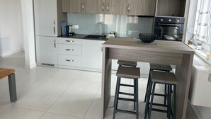 Eine moderne Küche mit Holzschränken, einer schwarzen Arbeitsplatte und einem eingebauten Backofen. Zwei Hocker stehen an der Kücheninsel.