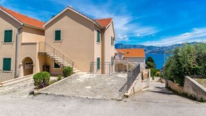 Un edificio costero con una escalera de piedra que lleva a un balcón, cielo azul despejado y vista al mar.