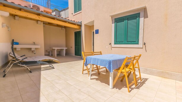 Un patio soleado con una mesa y sillas, una silla reclinable y una mesita con mantel azul.