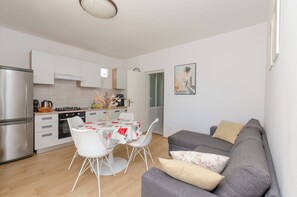 A modern kitchen with white cabinets, a dining table with chairs, and a grey sofa. - Apartments Big (Vodice)
