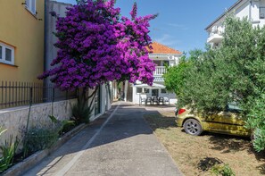 A narrow street with a yellow building on the left, a white building with a balcony on the right, and a car parked on the right side. - Apartments Big (Vodice)
